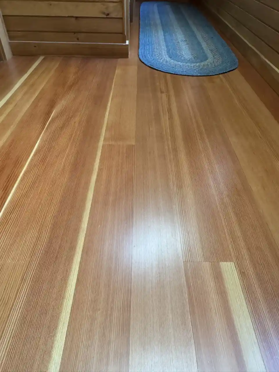 A low-angle photo of a newly refinished hardwood floor with visible wood grain and light reflections, featuring a blue…