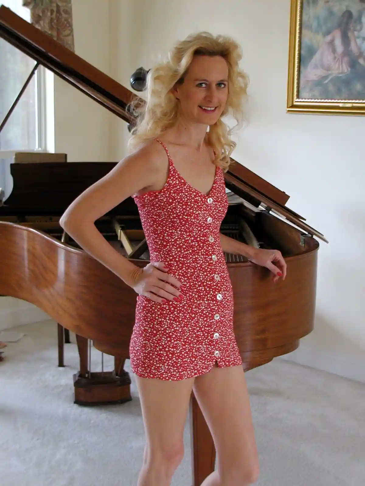 a woman with blonde curly hair wearing a red and white polka dot button-up dress stands confidently with one hand on her hip…