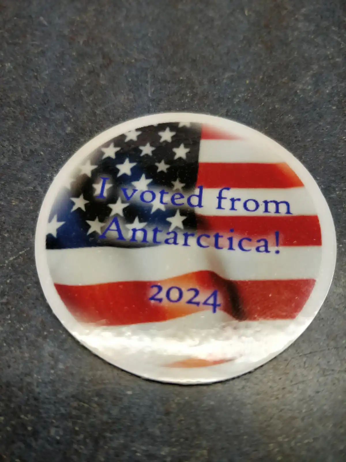 A circular button with a U.S. flag design displays the text 'I voted from Antarctica! 2024' in blue lettering. The button…