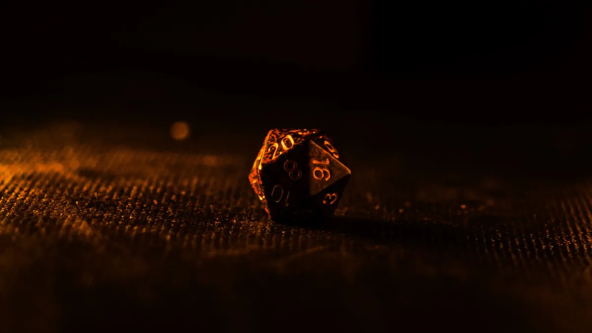 A black twenty-sided die with glowing orange numbers rests on a textured surface under warm, dim lighting. The die shows the…