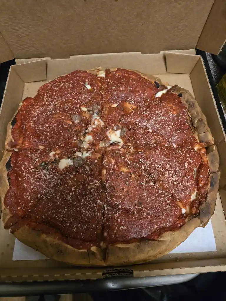 A deep-dish pizza with a thick crust, tomato sauce, cheese, and meat toppings, cut into slices and sitting in an open…