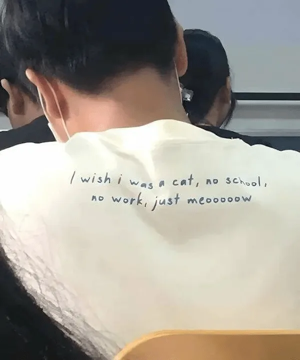 The back of a person wearing a white t-shirt with handwritten text that reads 'I wish i was a cat, no school, no work, just…