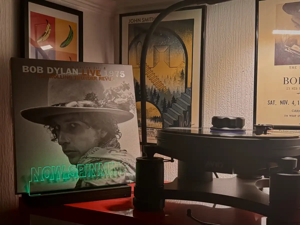 A vinyl record player sits on a red surface with a Bob Dylan 'Live 1975' album cover standing upright beside it. The album…