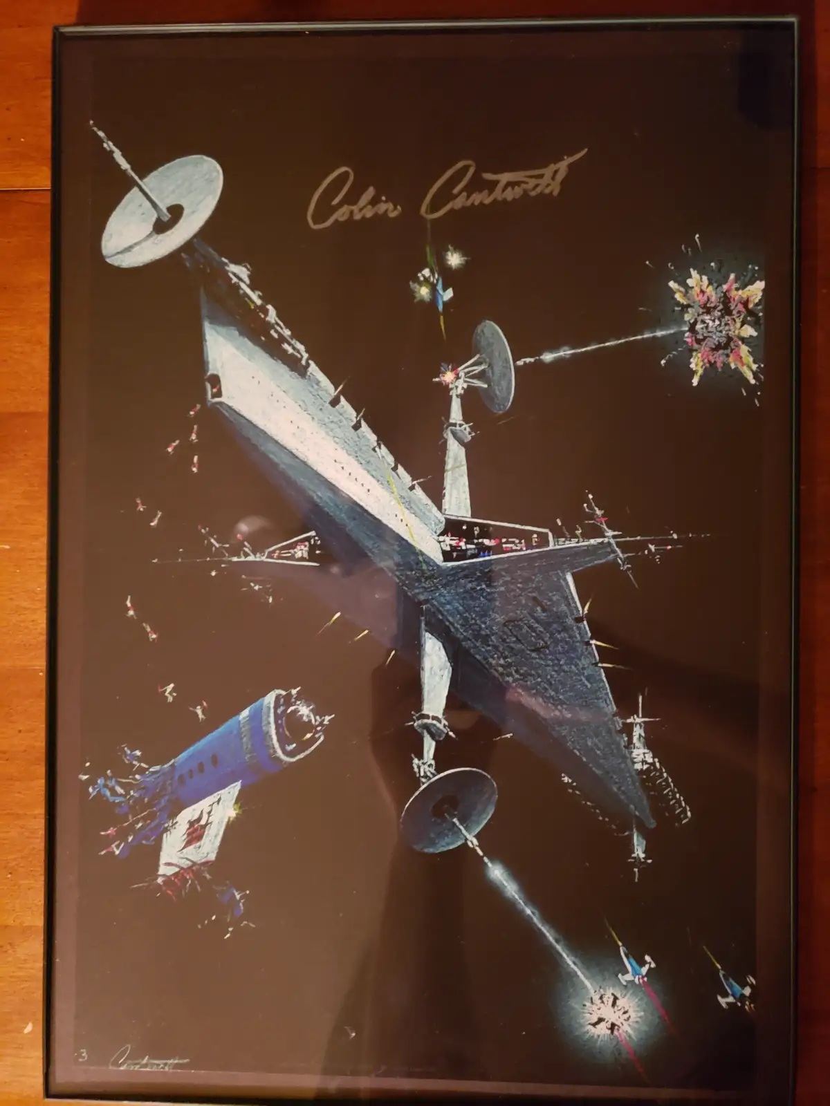 A framed vintage science fiction artwork depicts a large, angular spaceship engaged in battle, firing beams at smaller ships…