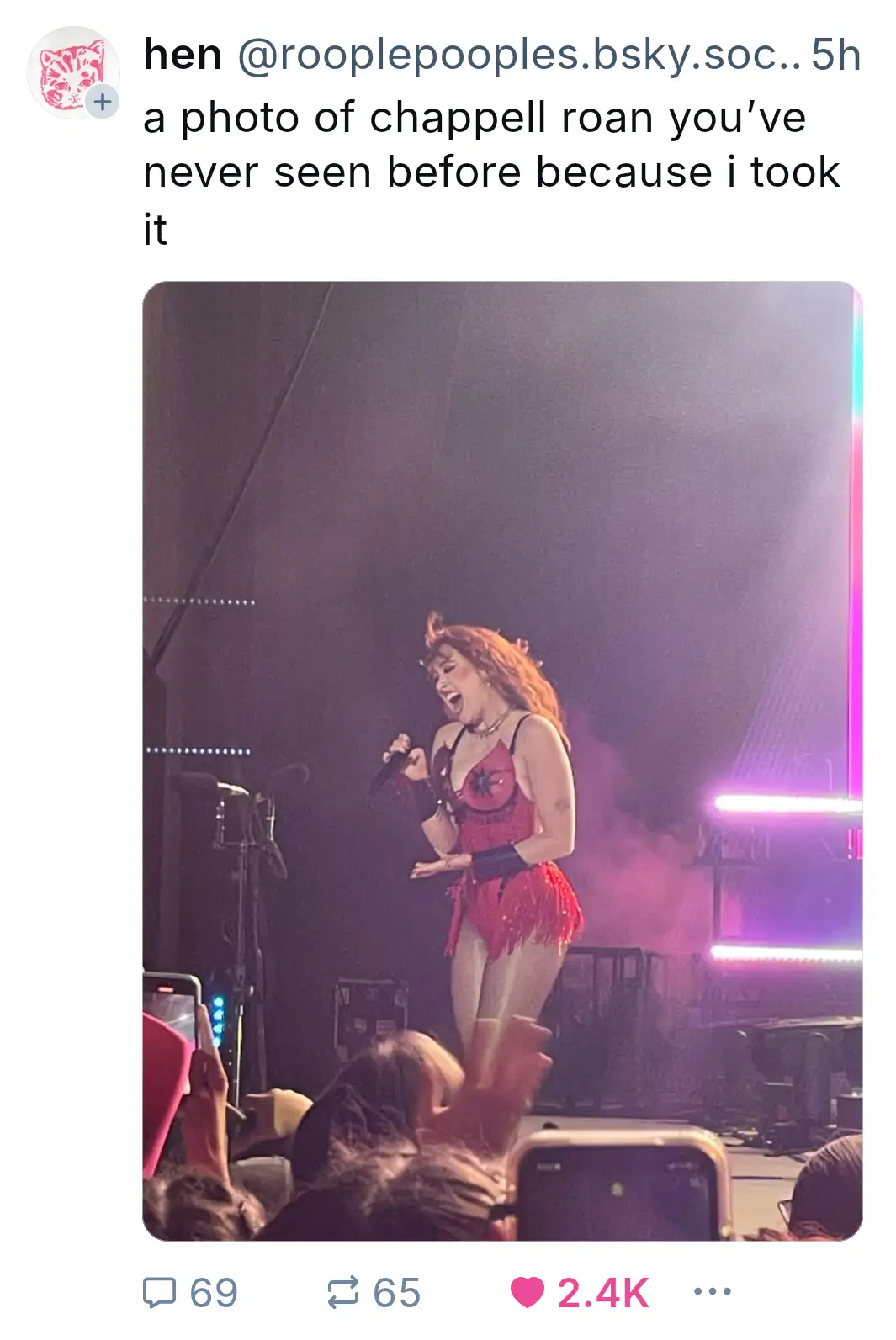 A photo of singer Chappell Roan performing live on stage in a red fringed outfit, holding a microphone and singing with her…