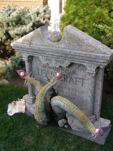 A weathered stone tombstone with engraved text reading 'HOWARD PHILLIPS LOVECRAFT 1890-1937 THE OLD AND STRONGEST FEAR IS…