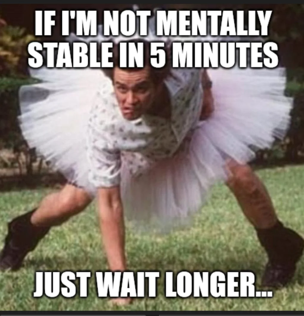 A man wearing a white tutu and black boots is crouched low on a grassy lawn, looking intensely at the camera. The image has…