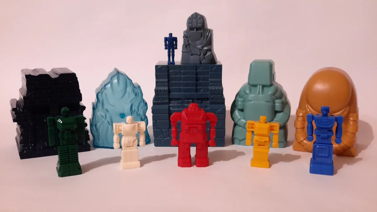 A row of colorful, blocky plastic robot toys stands in front of various themed plastic backdrops like ice, stone, and lava…