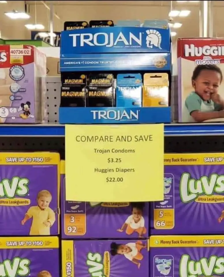 A store shelf displays boxes of Trojan condoms stacked above a yellow sign comparing their price to Huggies diapers. The…