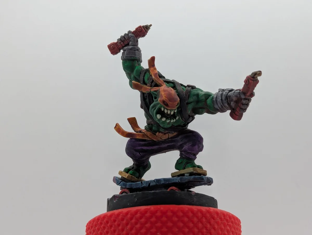 A painted green fantasy miniature of a muscular, horned, snarling humanoid figure with purple pants and armor, standing on a…