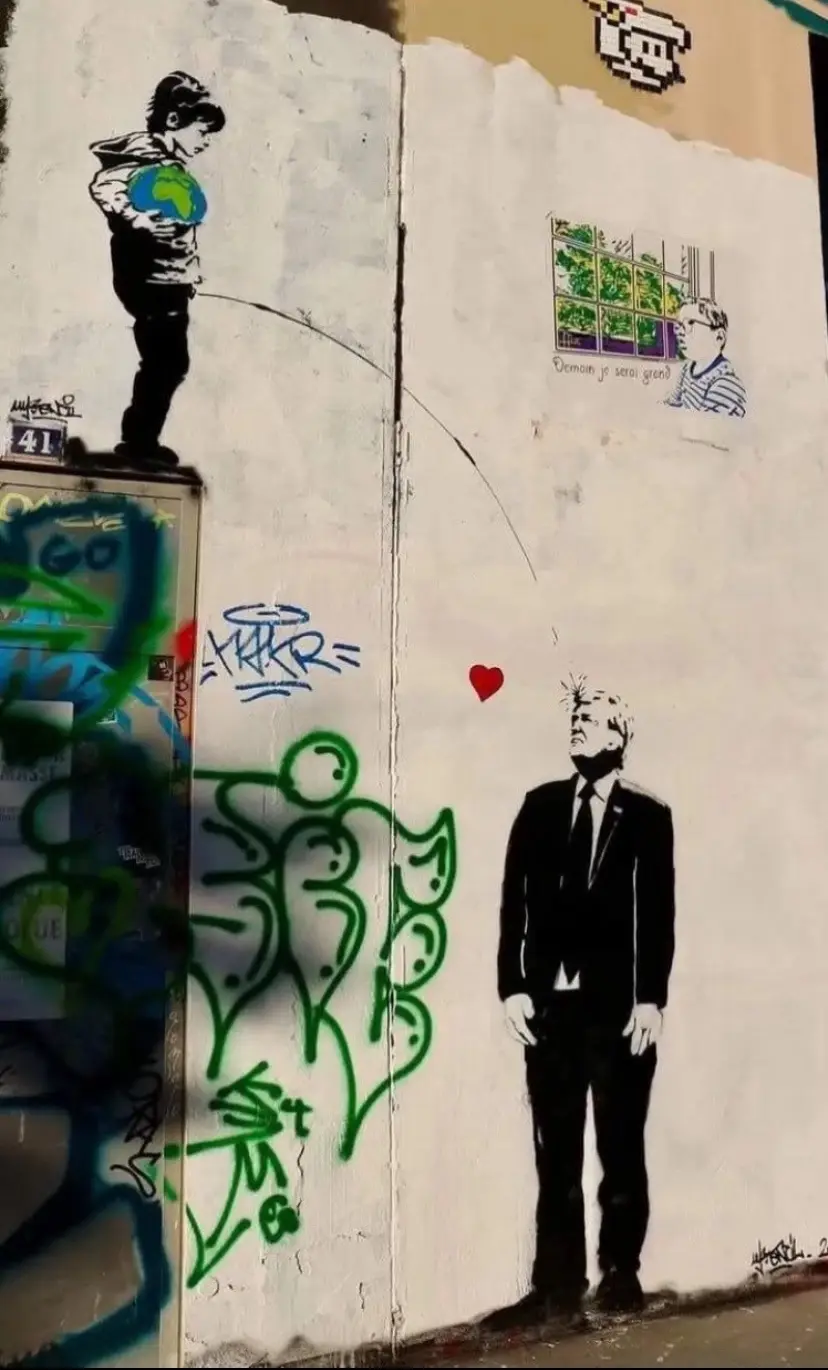 A street art mural shows a boy holding a globe on the left, fishing with a line that ends in a red heart above a man in a…