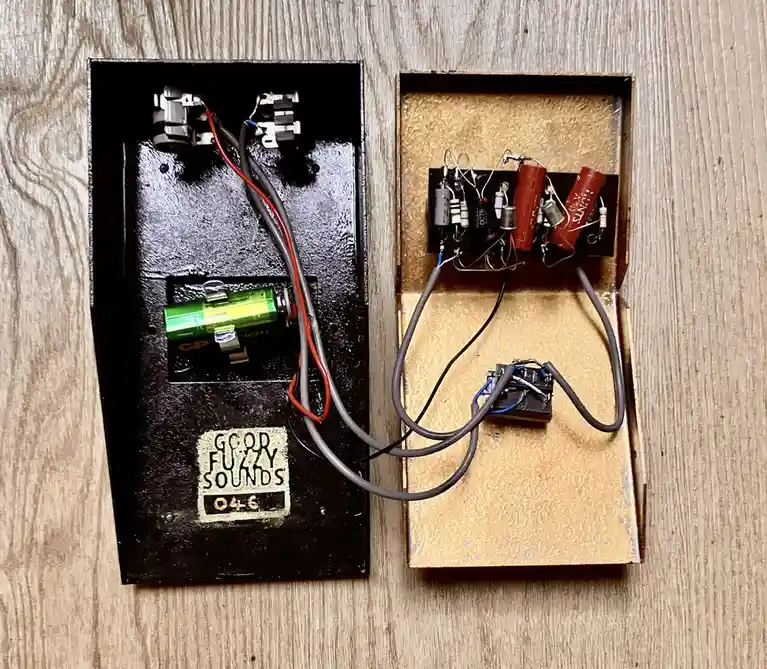 Two open electronic devices sit side-by-side on a wooden surface, revealing their internal circuitry. The left device has a…