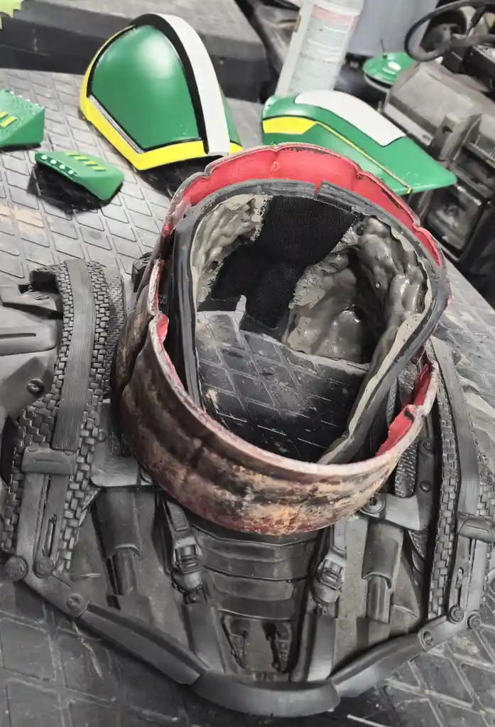 A close-up photo shows the inside of a worn, red-rimmed helmet with gray foam padding and black fabric lining, resting on a…