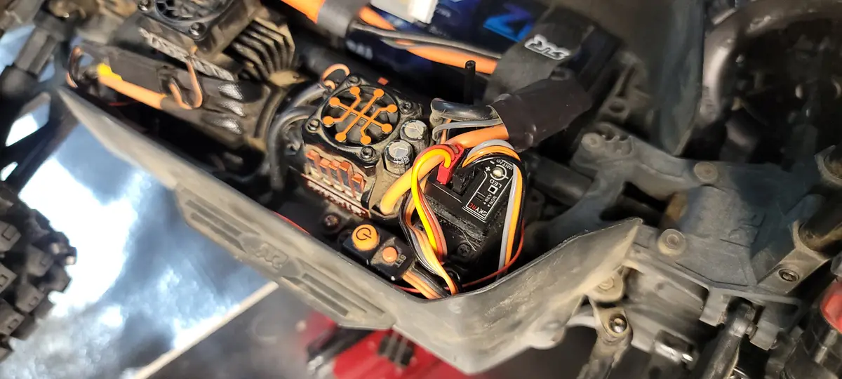 A close-up photo of the internal electronics of a remote-controlled car, showing a motor, ESC (electronic speed controller)…