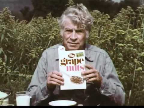 An older man with gray hair sits outdoors holding a box of 'grape nuts' cereal, with a glass of milk and a plate in front of…
