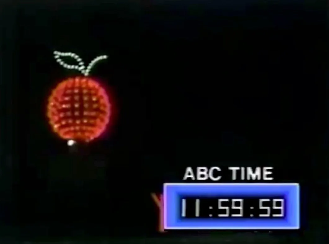 A dark background features a glowing red apple-shaped sign with a green stem and leaf, next to a blue digital clock…
