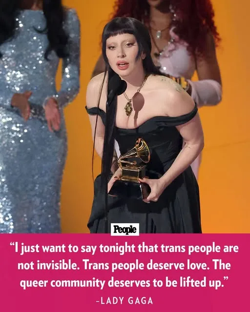 Lady Gaga stands on a stage holding a Grammy award, wearing a black off-the-shoulder dress and a necklace, with two other…