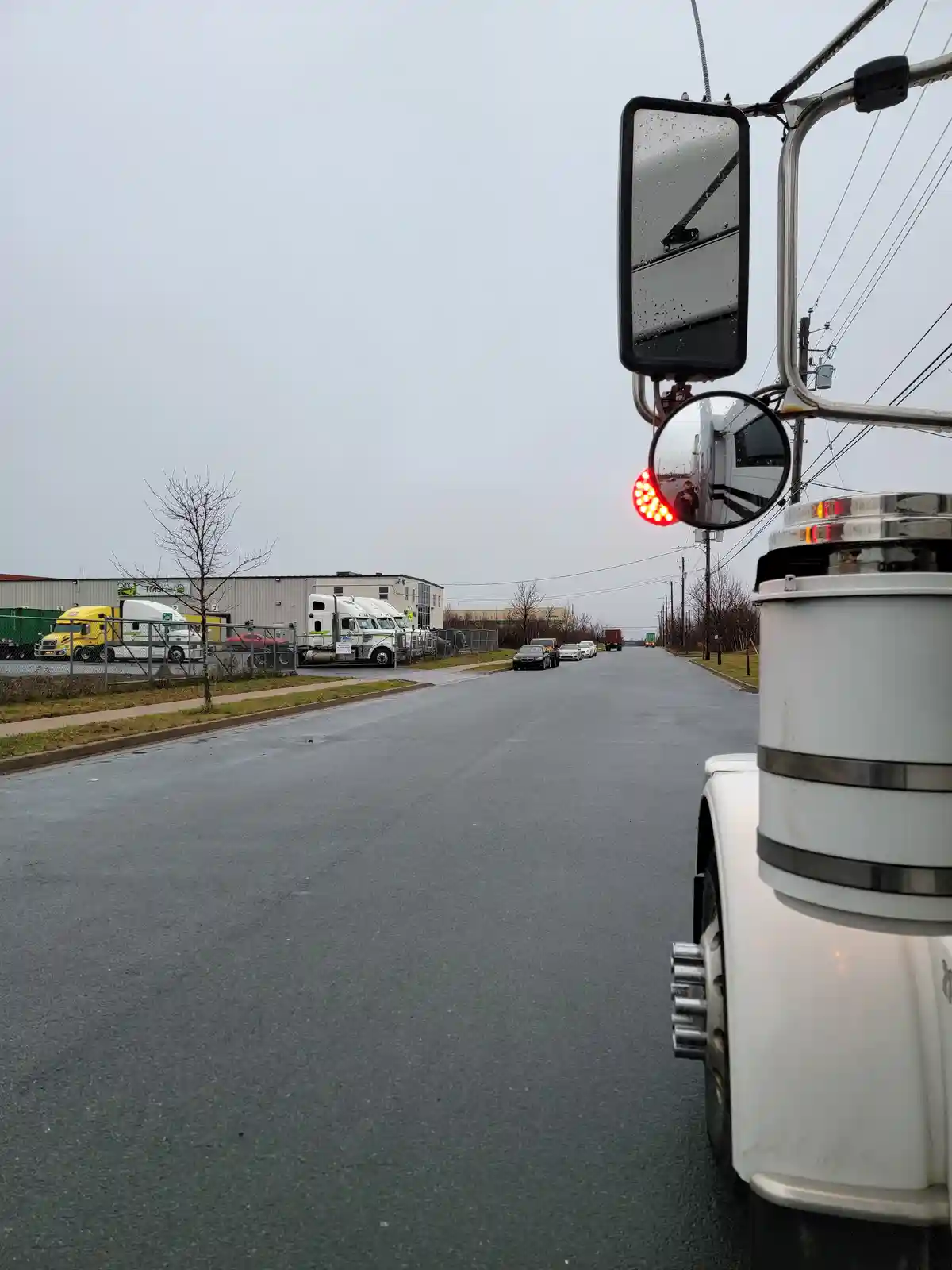 A photo taken from the side of a white semi-truck shows its large side mirror and smaller convex mirror. The convex mirror…