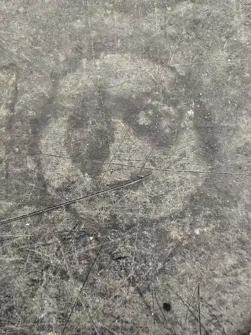 A close-up of a heavily scratched and worn gray surface, possibly a cutting board or countertop, with a faint circular stain…