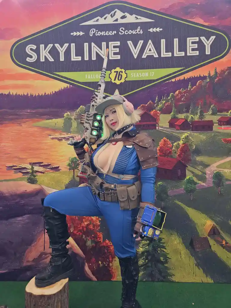 A person in a Fallout 76 Pioneer Scout cosplay poses confidently in front of a promotional backdrop for Skyline Valley…