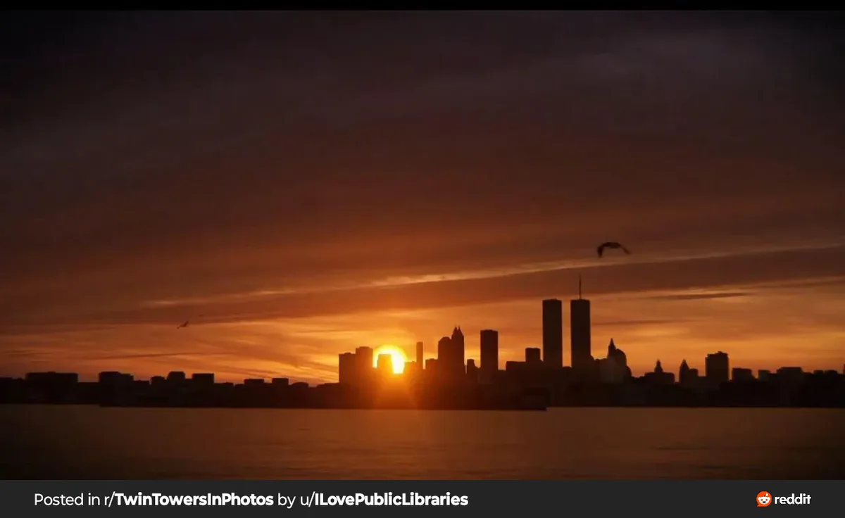 A sunset photo of the New York City skyline with the Twin Towers visible, the sun setting behind them, and birds flying in…