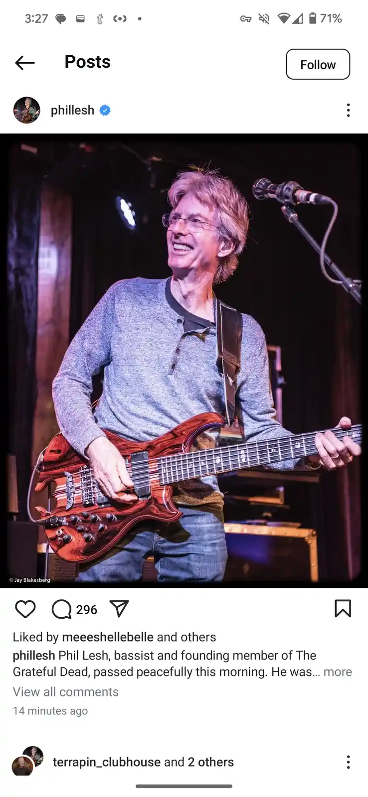 A photograph of Phil Lesh, bassist and founding member of The Grateful Dead, smiling while playing a red electric bass…