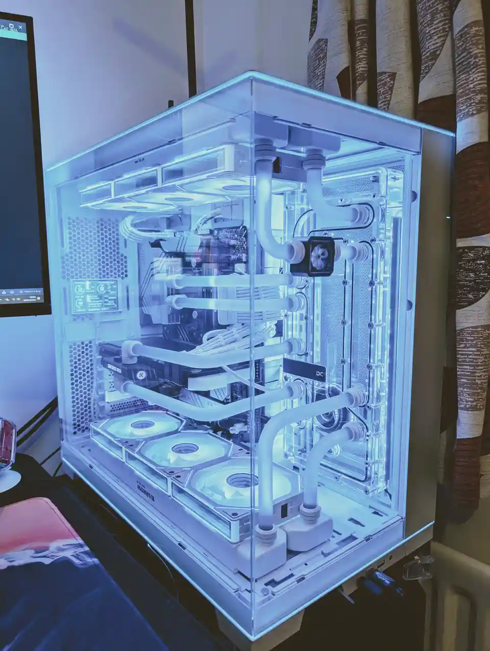 A custom-built computer with a transparent case and intricate white liquid cooling tubes glowing under blue LED lights, with…