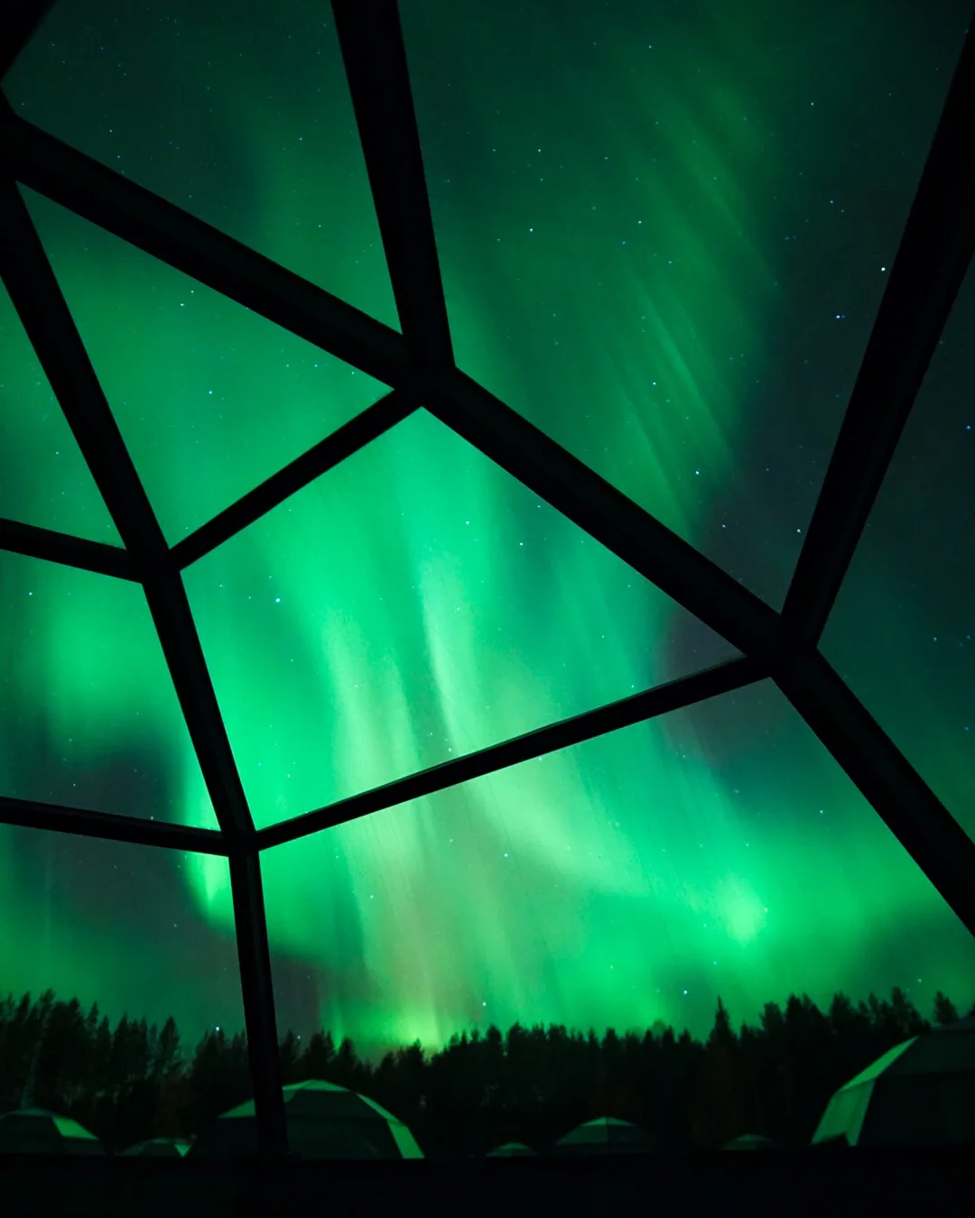 A stunning view of vibrant green northern lights dancing across a starry night sky, framed by the dark geometric structure…