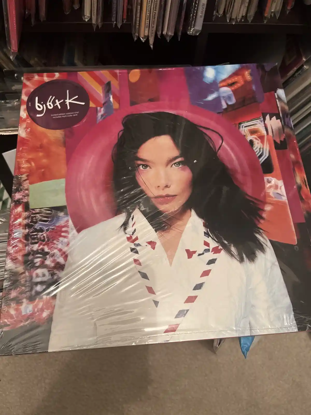 A close-up photo of a sealed vinyl record album cover featuring a woman with dark hair and a white jacket with red and blue…