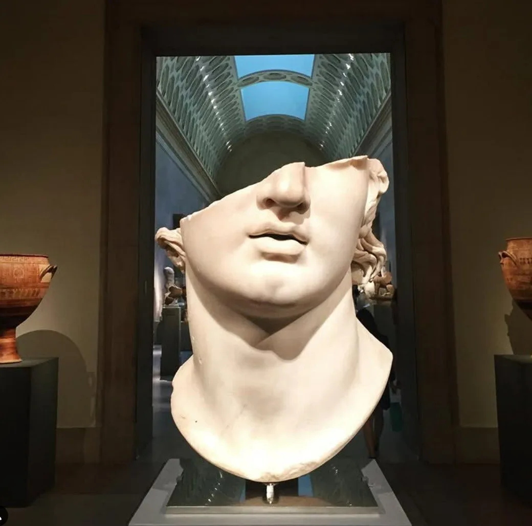 A marble bust of a classical figure is displayed in a museum, but its eyes are missing, creating a humorous visual pun. The…