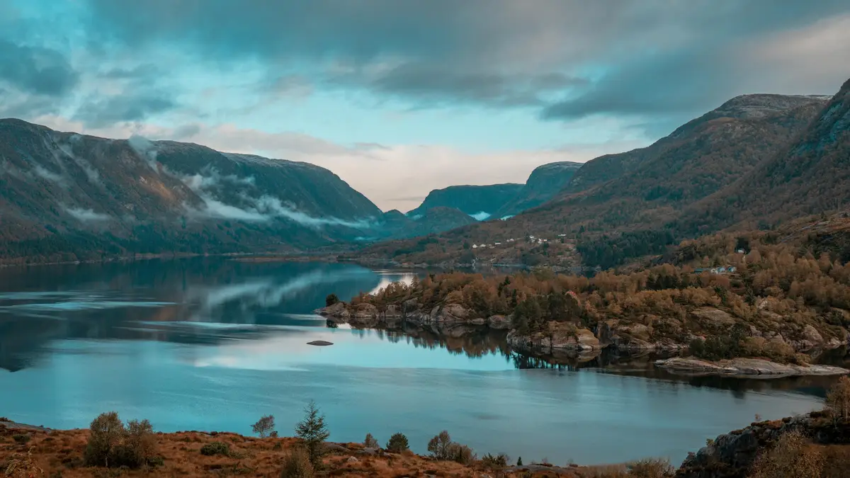 Crystal clear waters reflect the misty hills, as wispy clouds drift lazily across the Norwegian sky, casting dappled shadows…