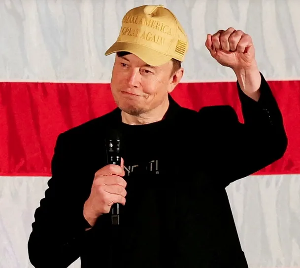elon musk wearing a yellow 'make america great again' cap, holding a microphone, and raising his fist in front of an…