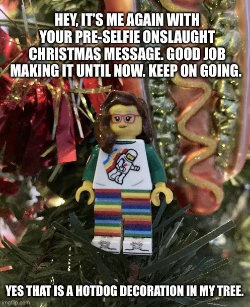 A lego minifigure with brown hair and glasses, wearing a white t-shirt with a rainbow and astronaut graphic, rainbow-striped…