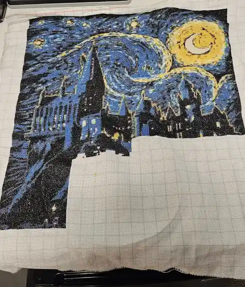A partially completed cross-stitch project depicts Vincent van Gogh's 'Starry Night' with swirling blues and yellows, but…