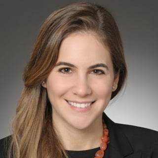 A professional headshot of a smiling woman with brown hair, wearing a black blazer and an orange beaded necklace, overlaid…