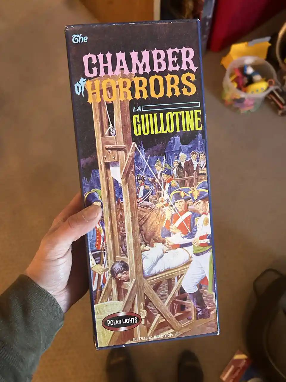 A hand holds a vintage Polar Lights 'Chamber of Horrors' plastic model kit box featuring a guillotine execution scene with…