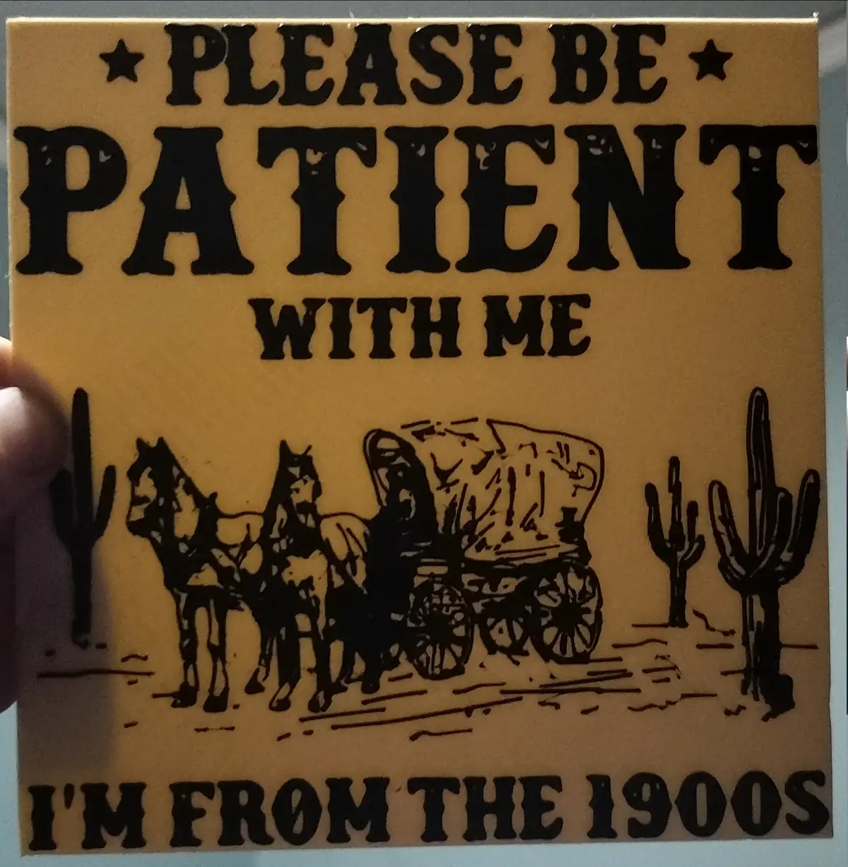 A tan-colored sign with black text and illustration depicts a covered wagon pulled by two horses in a desert with cacti. The…