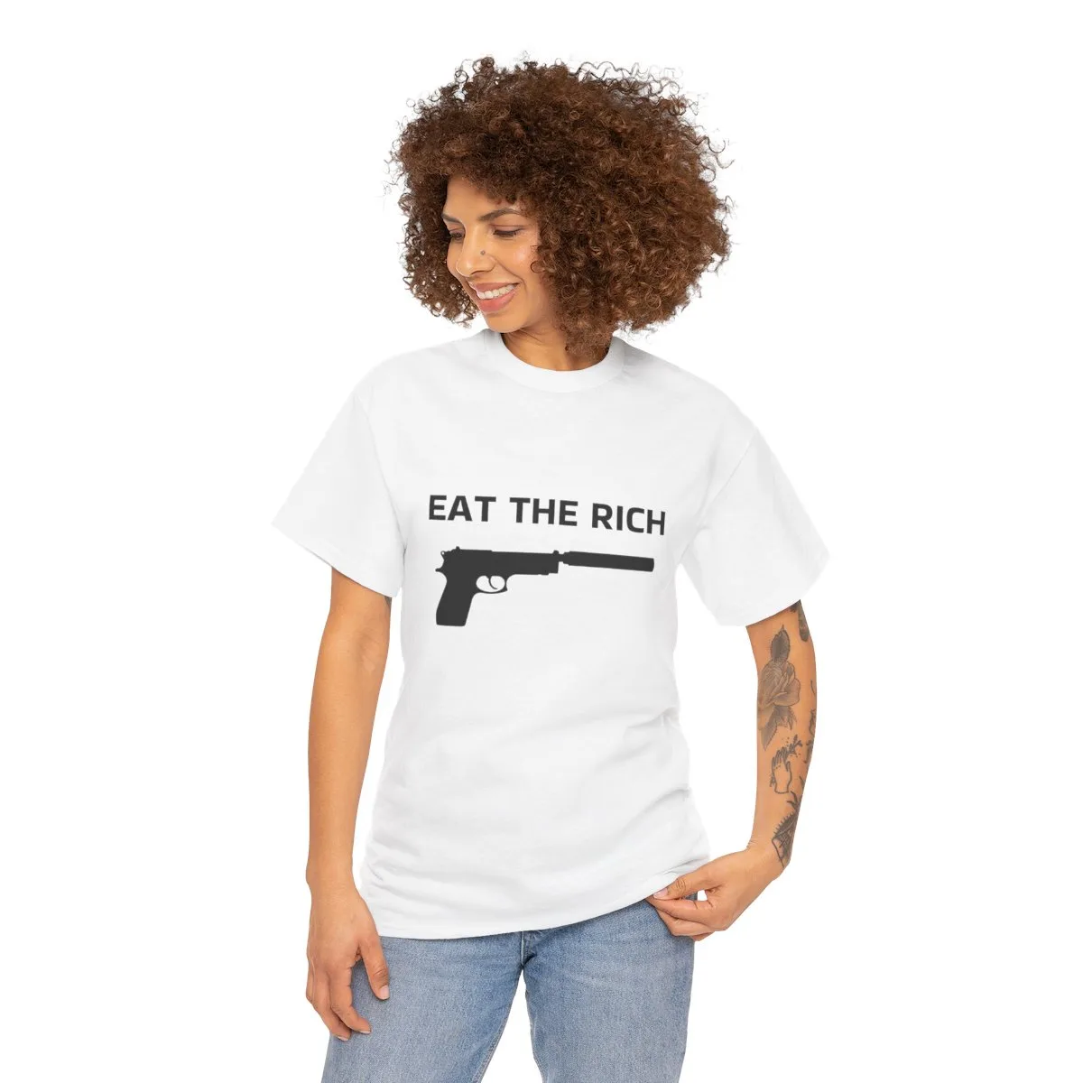 A woman with curly brown hair and tattoos on her right arm wears a white t-shirt with the text 'EAT THE RICH' printed above…