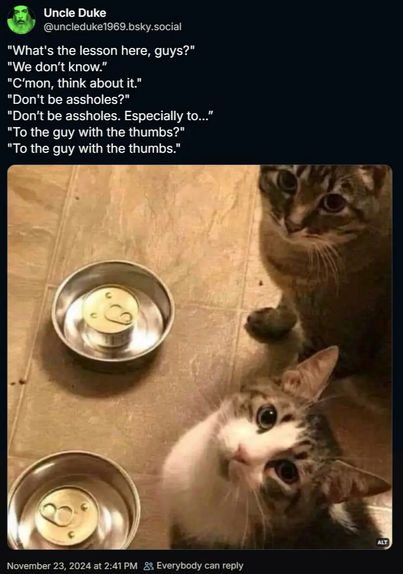 Two cats stare up at the camera from a tiled floor beside two metal bowls, each containing an upside-down can of food. The…