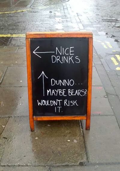 A wet sidewalk chalkboard sign directs customers to 'NICE DRINKS' with an arrow pointing left, while an arrow pointing up…