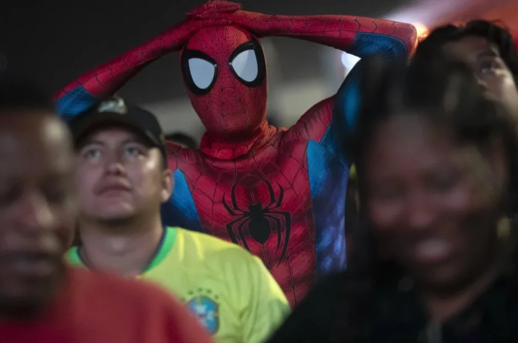 A person in a full Spider-Man costume stands among a crowd, hands clasped over their head in a gesture of exasperation or…