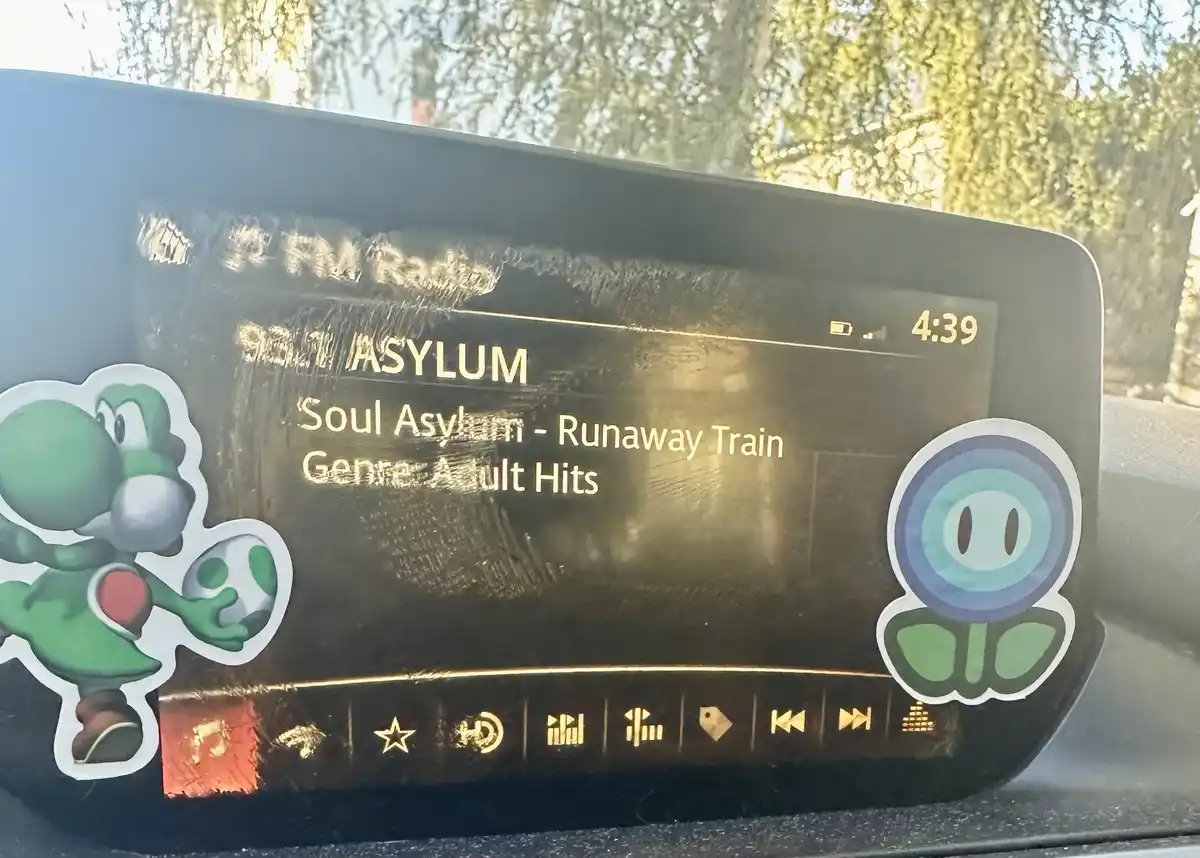 A car's infotainment screen displays the radio station '93.1 ASYLUM' playing 'Runaway Train' by Soul Asylum, categorized as…