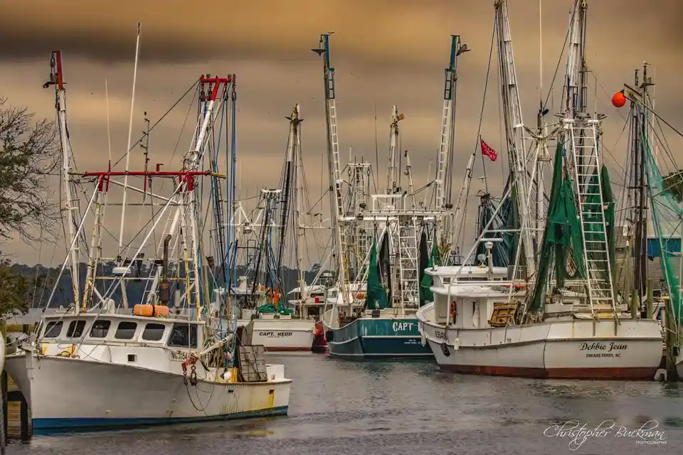 A photograph of several fishing boats docked in a harbor under a cloudy sky, with visible names like 'Debbie Jean' and…