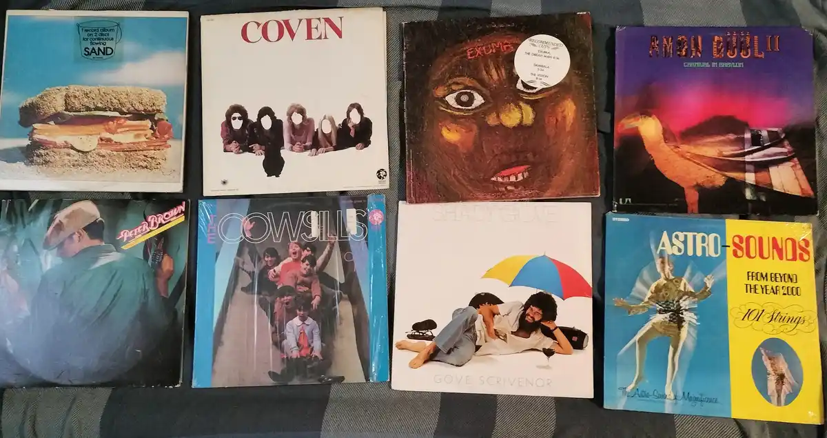 Eight vintage vinyl record album covers are laid out on a plaid fabric surface. The covers feature various artists and…
