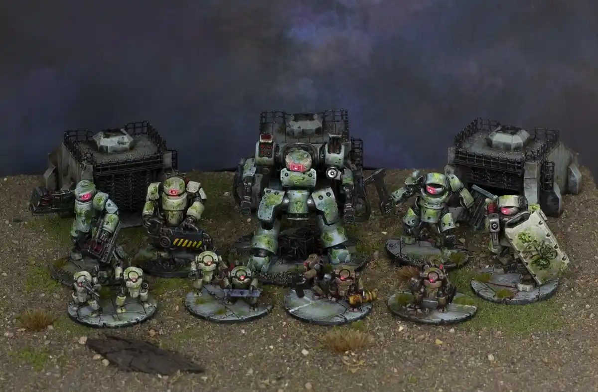 A collection of painted miniature robots and mech units, covered in moss and grime, stand on a dirt and grassy terrain with…