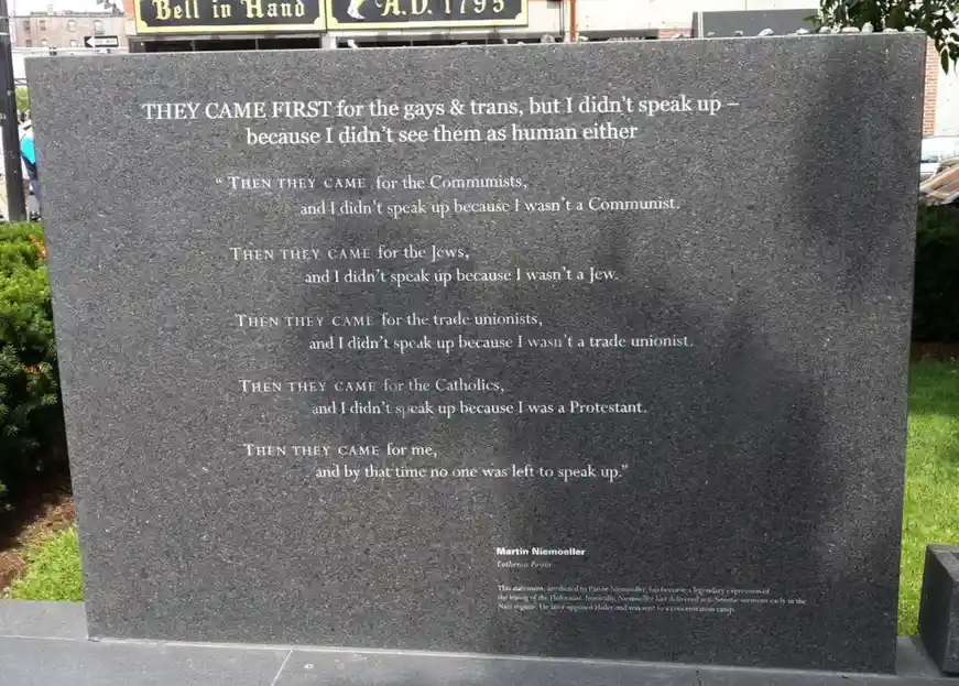 A dark gray stone monument displays a modified version of Martin Niemöller's famous quote, with the first stanza altered to…