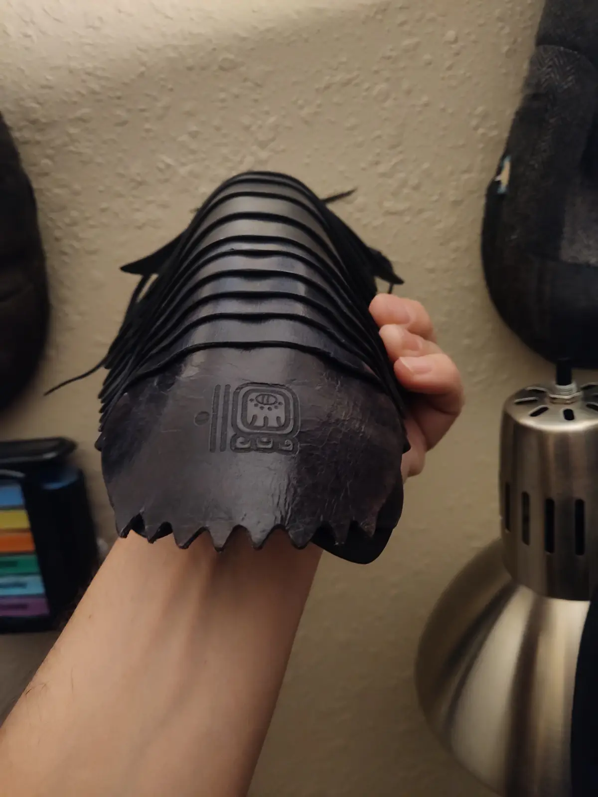 A person holds up a custom-made black leather gauntlet with a serrated edge and an embossed symbol, showing it off proudly…