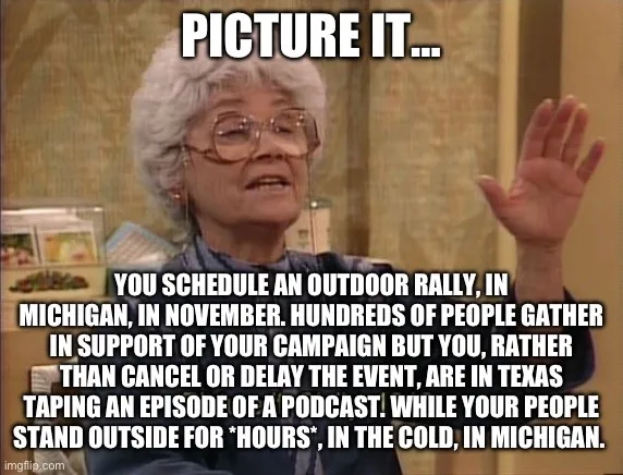 An older woman with white hair and glasses, wearing a blue shirt, gestures with her right hand while speaking. The image has…