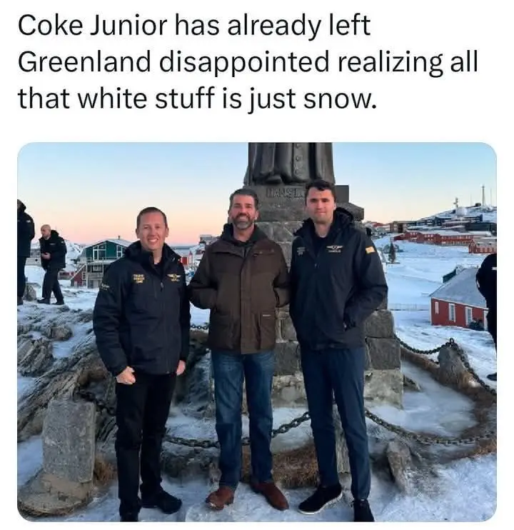 Three men in jackets stand in front of a monument in a snowy, Arctic-looking town with red buildings in the background. The…