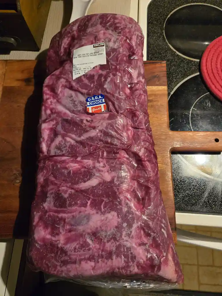 A large, vacuum-sealed package of frozen beef loin, labeled 'Kirkland Signature' and 'U.S.D.A. CHOICE Grade', rests on a…